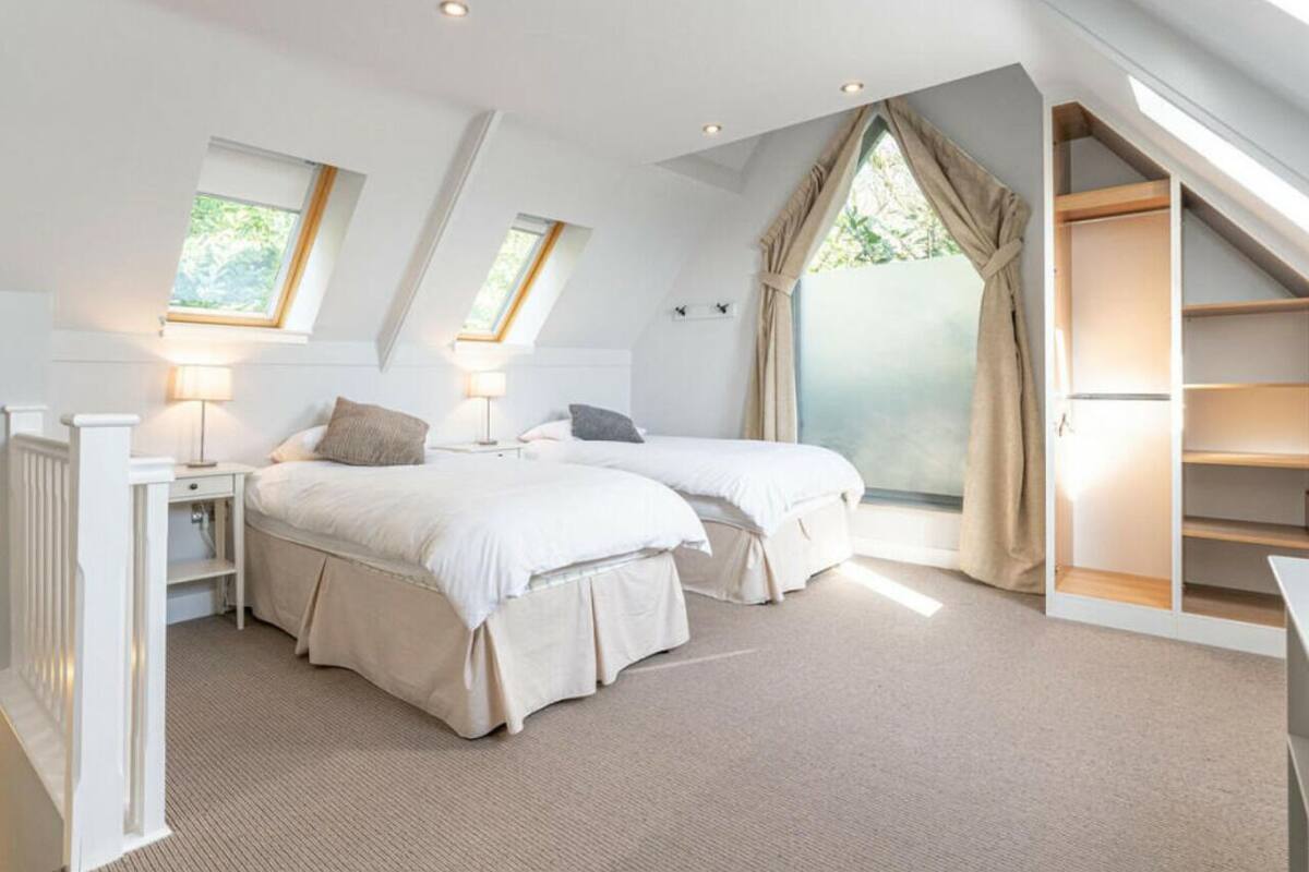 Une chambre avec deux lits, une lucarne, une fenêtre et une étagère intégrée.