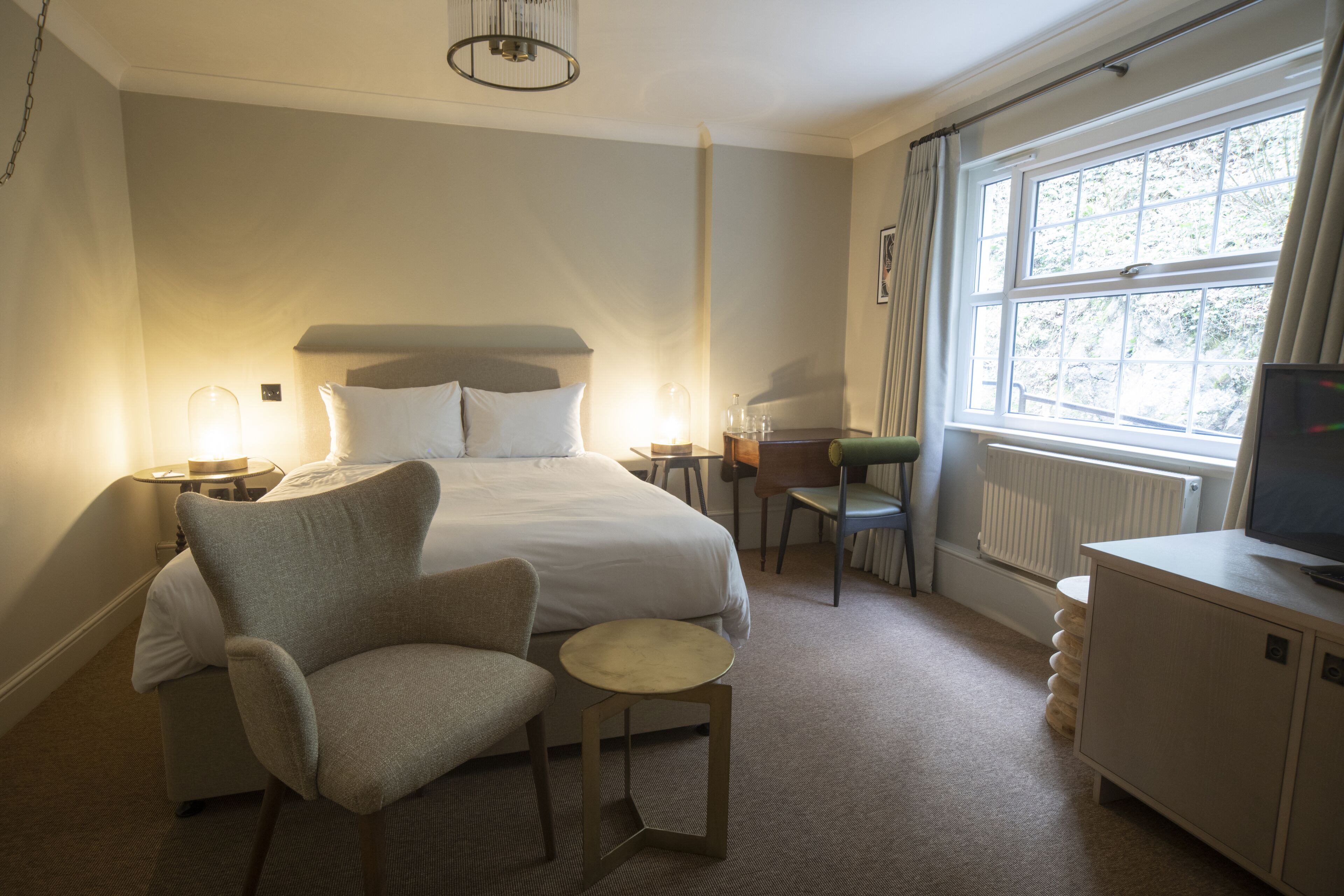 Ett hotellrum med en säng, en stol, ett litet bord, ett skrivbord och en tv.