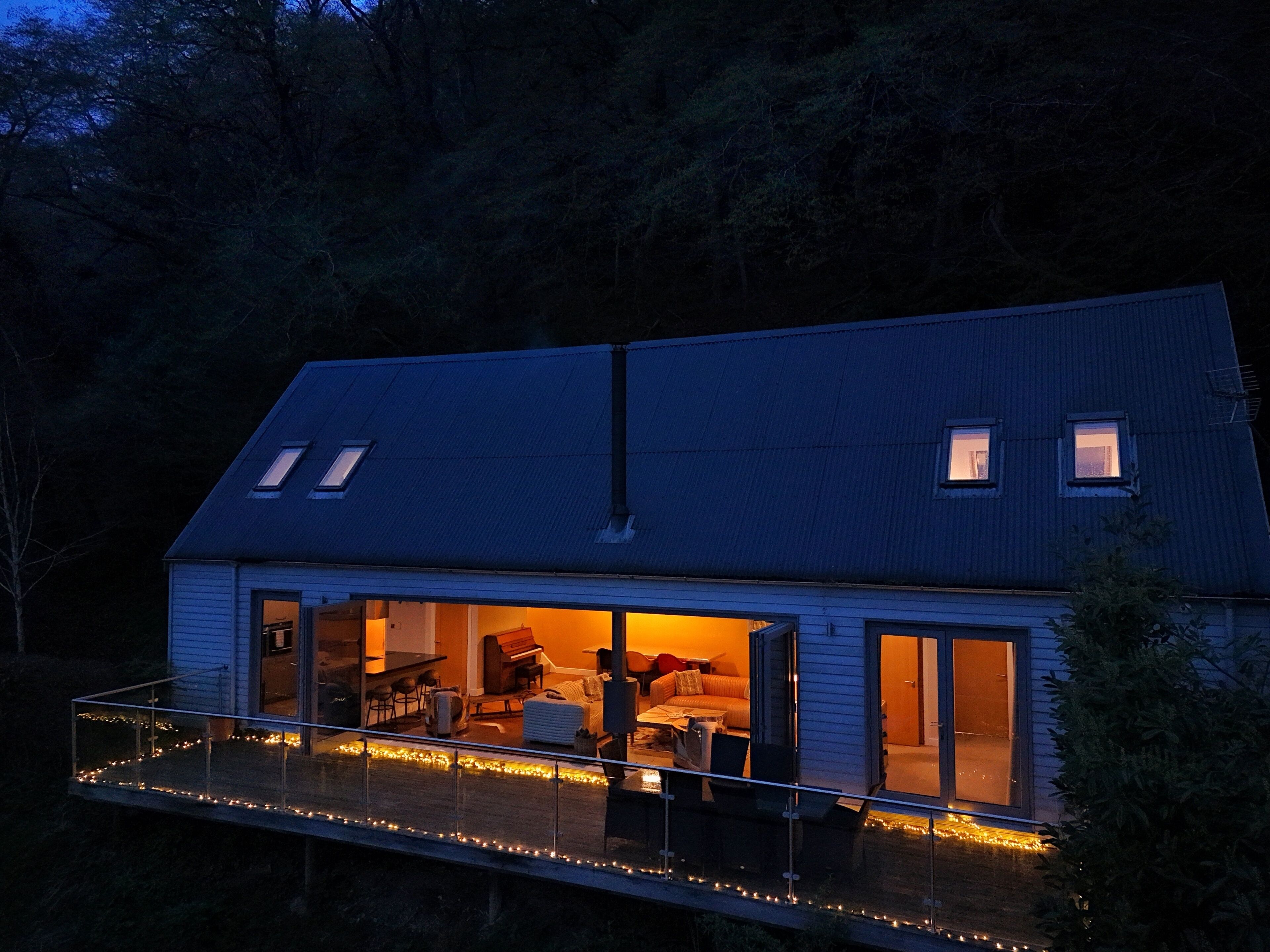 A modern house with a balcony, large windows, and a warm interior light.
