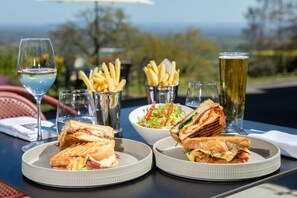 A table with two plates of sandwiches, a bowl of salad, and a glass of beer, set outdoors with a view. - The Cottage in the Wood (Malvern)