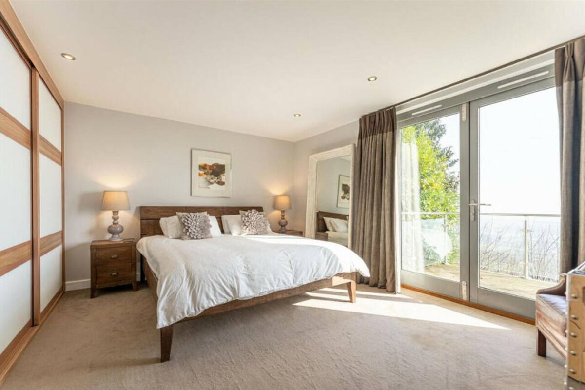 Une chambre avec un grand lit, deux tables de chevet avec des lampes, un grand miroir et une porte-fenêtre coulissante donnant sur un balcon.