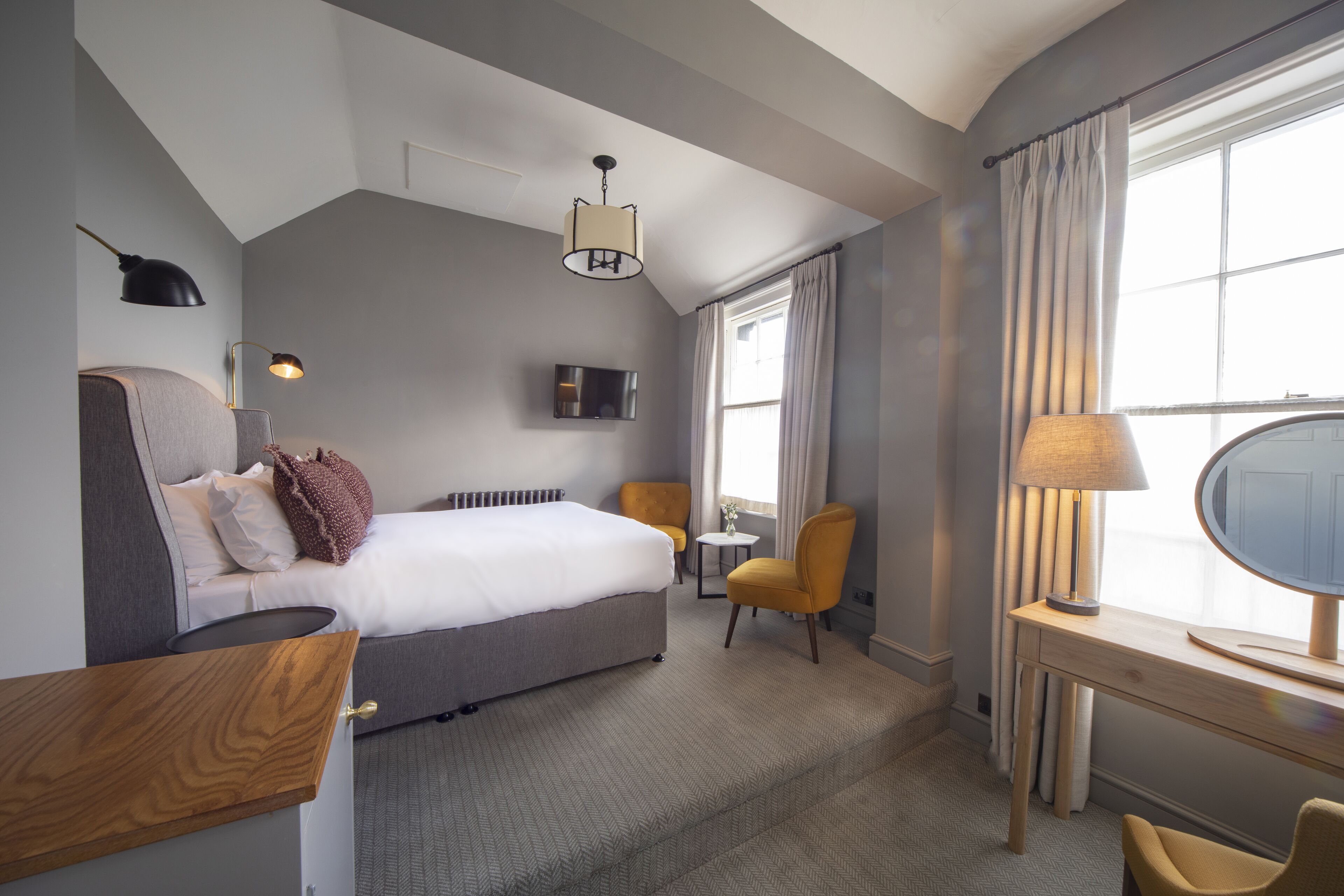 Habitación de hotel con cama, escritorio, silla, televisor y ventana con cortinas.
