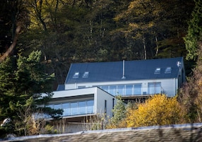 Una casa moderna de dos pisos con techo inclinado, ventanas grandes y una chimenea visible.