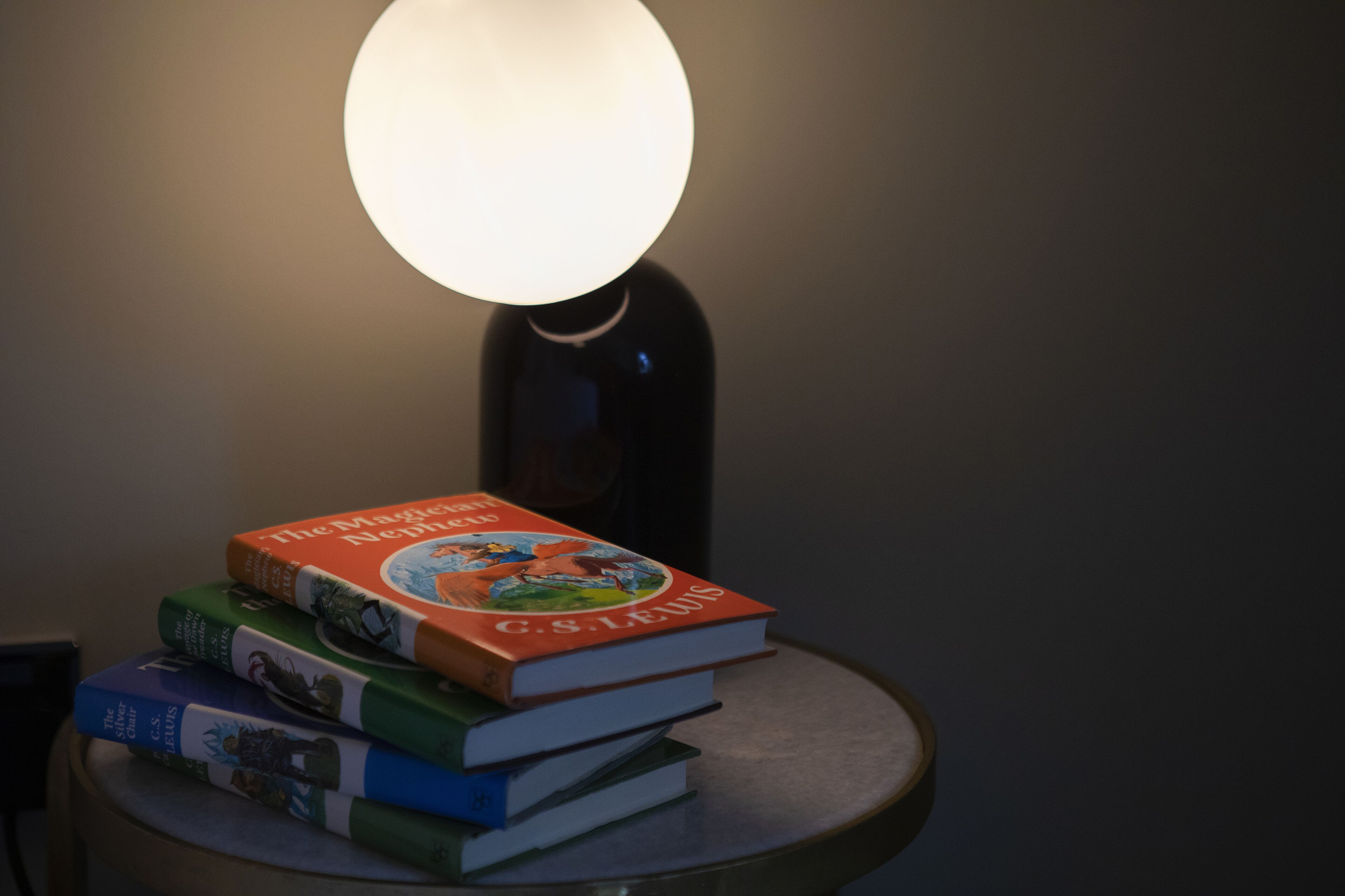 Un montón de libros sobre una mesa redonda con una lámpara que ilumina.