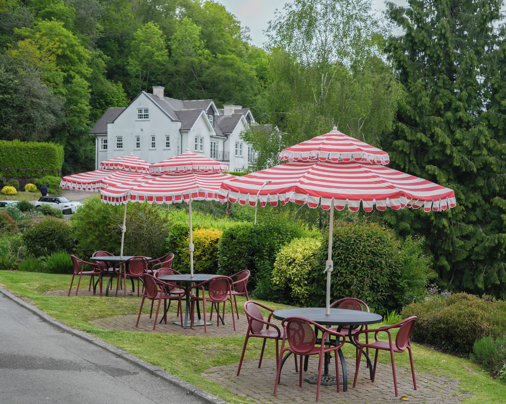 Outdoor seating with striped umbrellas, a paved patio, and a white building in the background.
