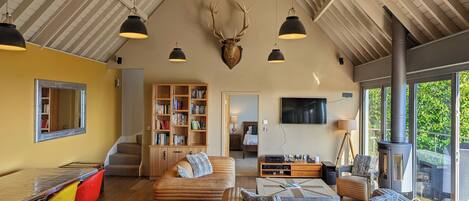 A spacious living area with a high ceiling, a fireplace, a television, and a bookshelf.
