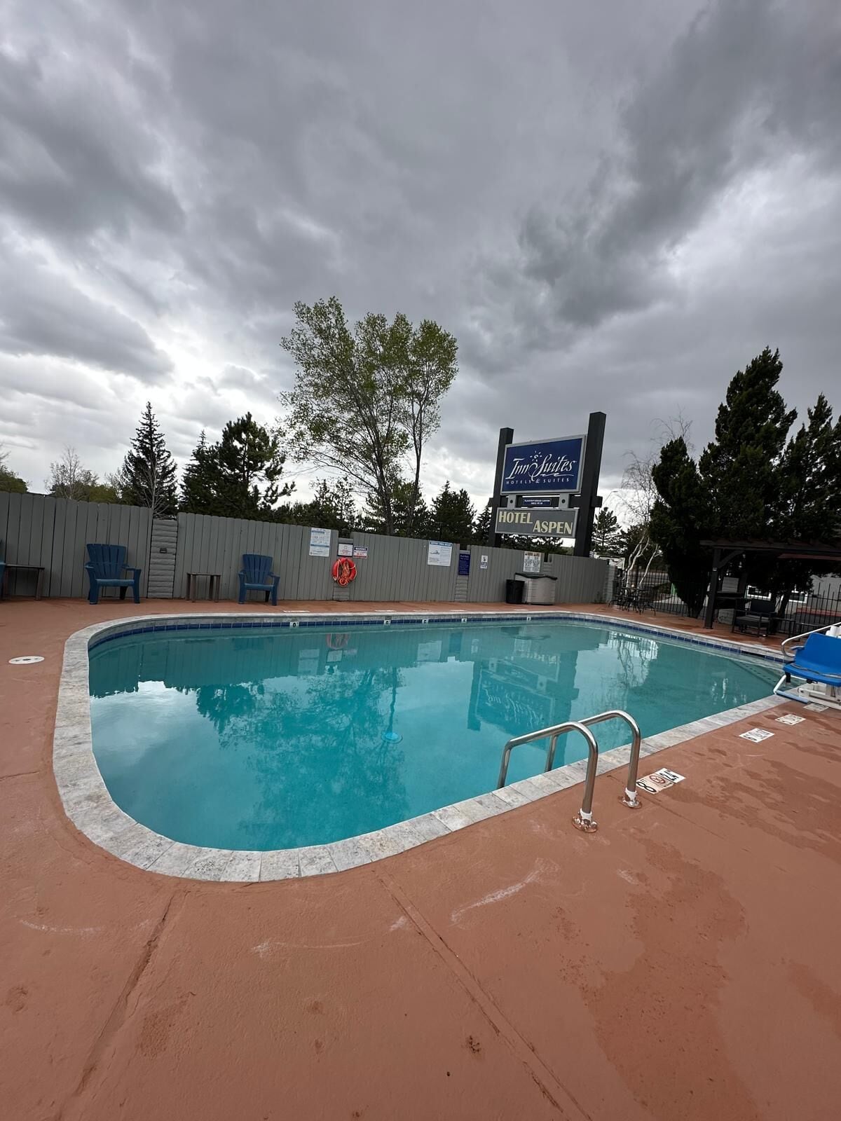 A swimming pool with a lifeguard chair, a sign for 'Tim Hortons Hotel & Suites,' and a fenced area with trees.