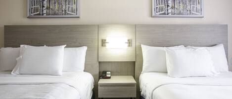 Hotelkamer met twee bedden, een nachtkastje met telefoon en lamp, en twee aan de muur hangende schilderijen van bomen.