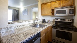 Una cocina con encimeras de granito, pileta de acero inoxidable, muebles de madera, un microondas y un horno.