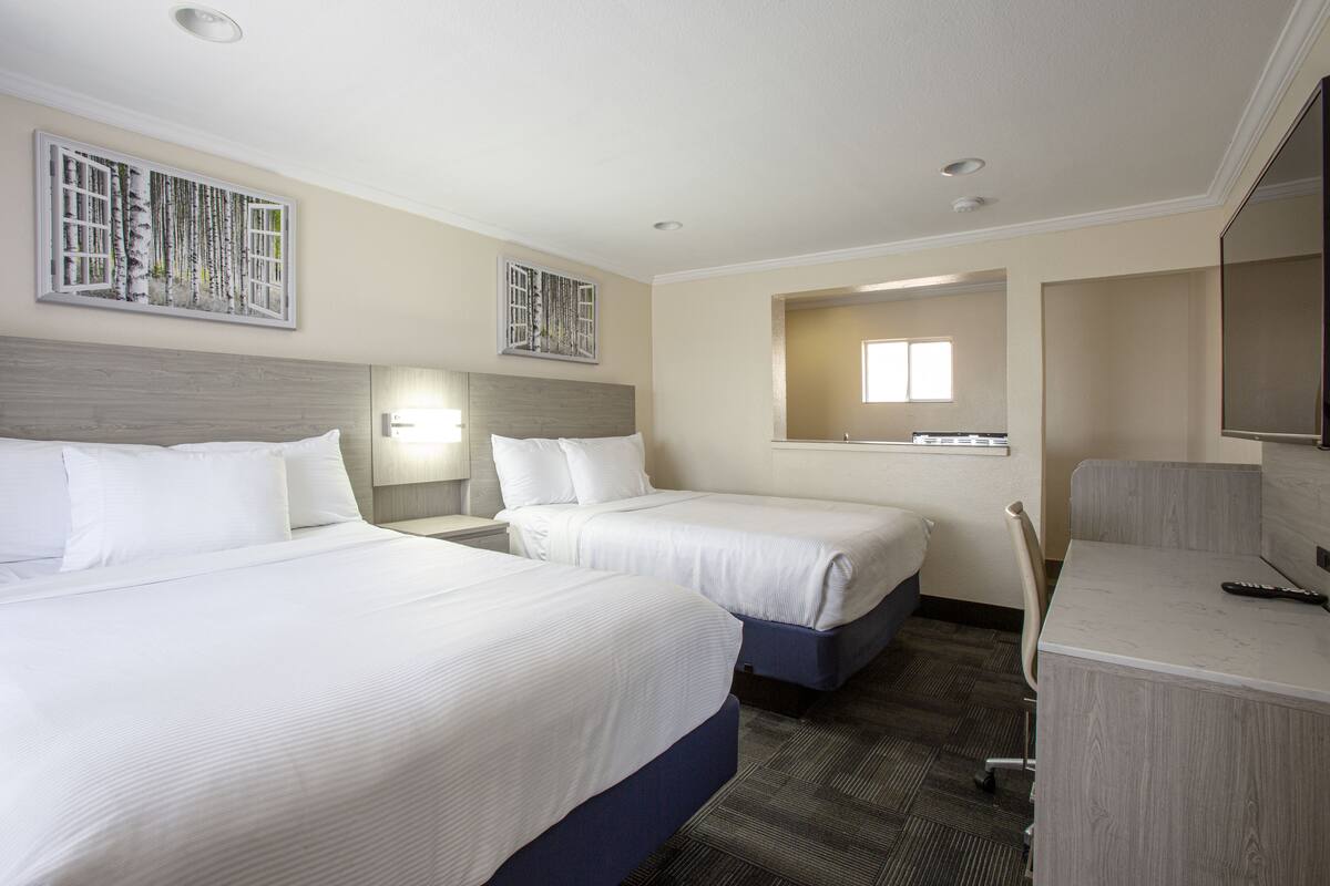 Habitación de hotel con dos camas, un escritorio, una silla y obras de arte en las paredes.