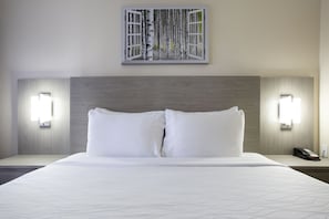 A hotel room with a large bed, two bedside lamps, a telephone, and a painting of birch trees on the wall.