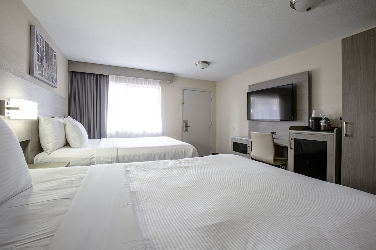 Habitación de hotel con dos camas, una televisión de pantalla plana, un escritorio con silla y una ventana con cortinas.