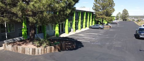 A parking lot with a row of parked cars, a building with green accents, and trees.
