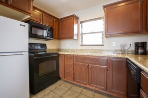 A kitchen with wooden cabinets, a black stove, a white refrigerator, a microwave, and a window with blinds. - Hotel Aspen InnSuites Flagstaff/Grand Canyon (Flagstaff)