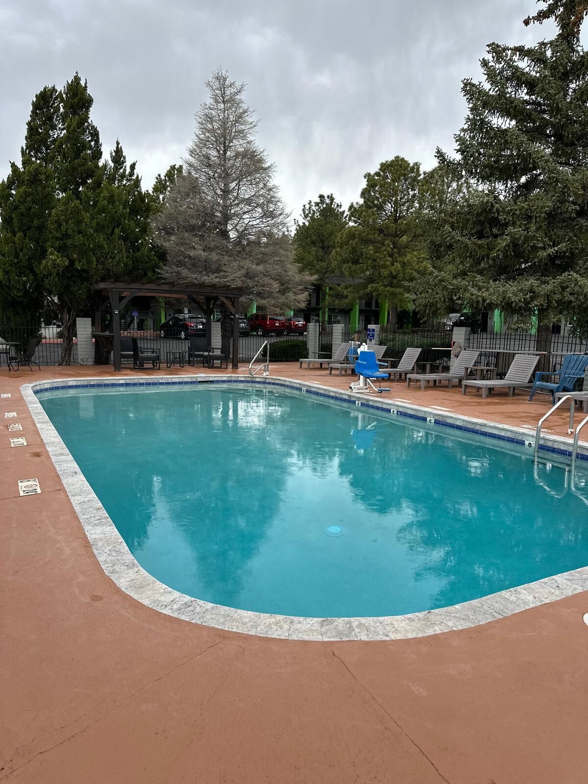 Une piscine dont le bord est revêtu de carrelage, entourée de chaises longues et d’un espace de repos abrité.