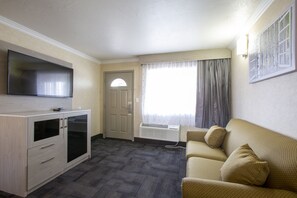 A hotel room with a flat-screen TV, a wooden cabinet, a sofa, and a large window with curtains. - Hotel Aspen InnSuites Flagstaff/Grand Canyon (Flagstaff)