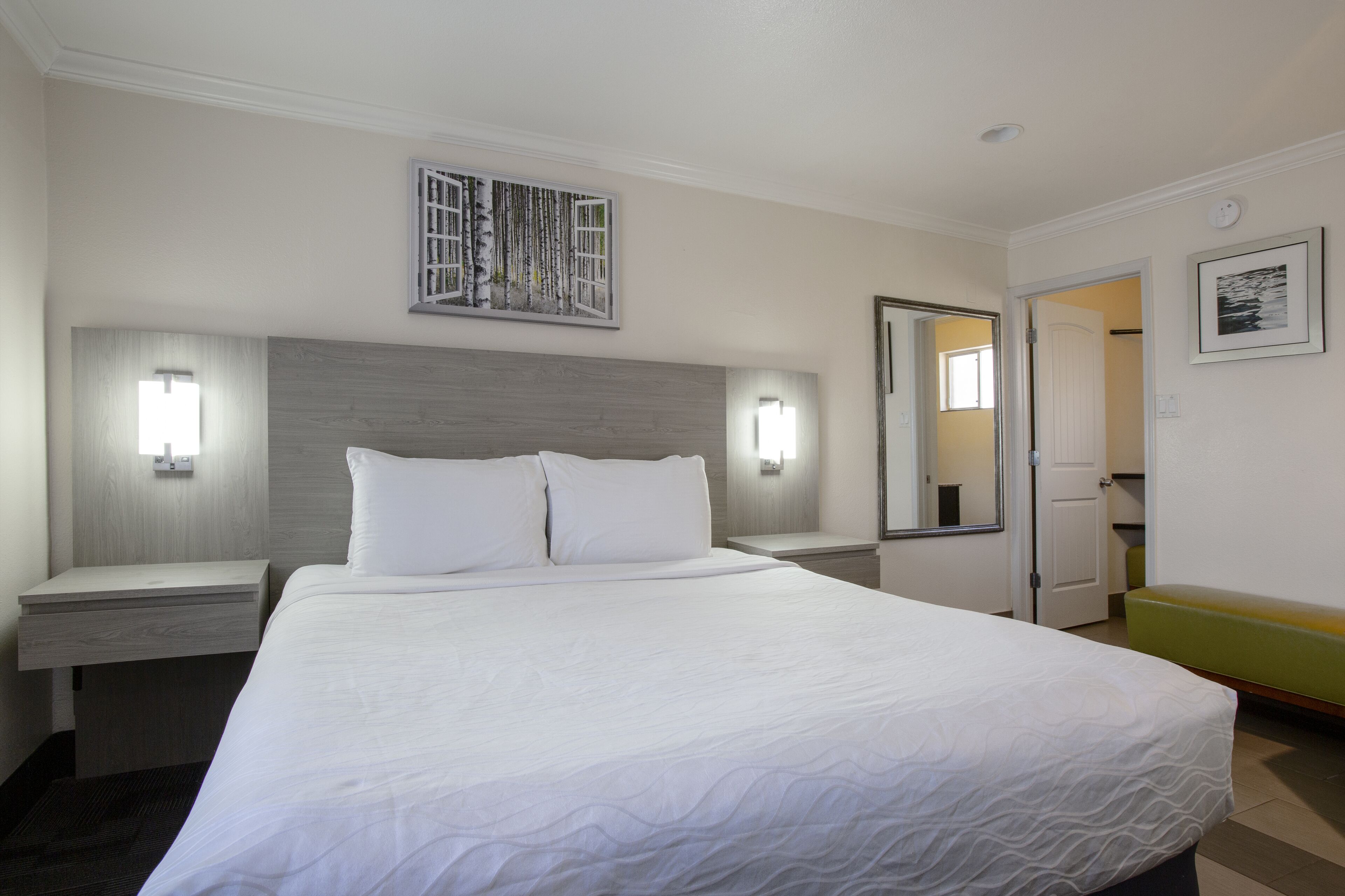 A hotel room with a large bed, bedside tables, a mirror, and a wall-mounted artwork.