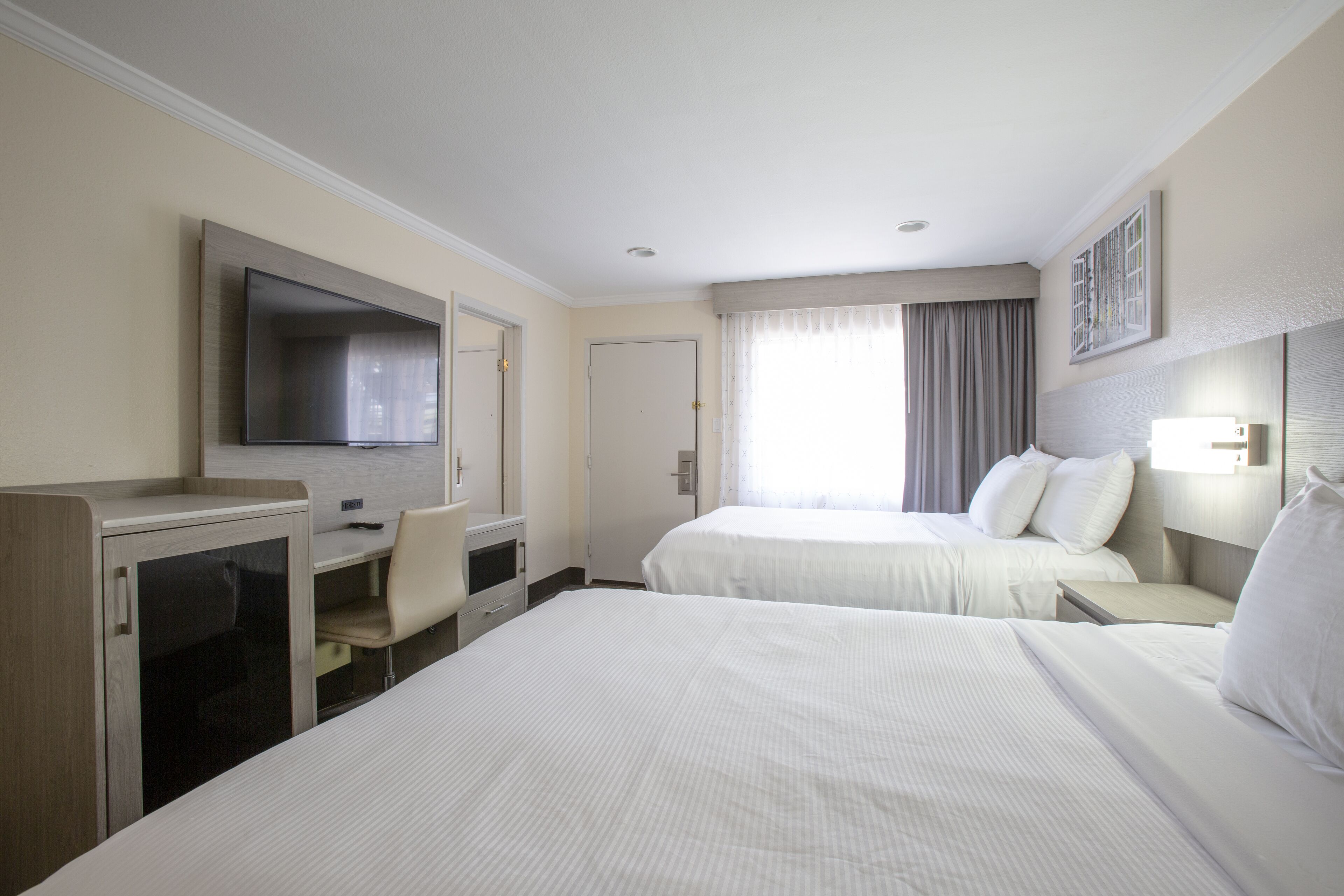 Habitación de hotel con dos camas, un escritorio, una silla, un televisor y una ventana con cortinas.