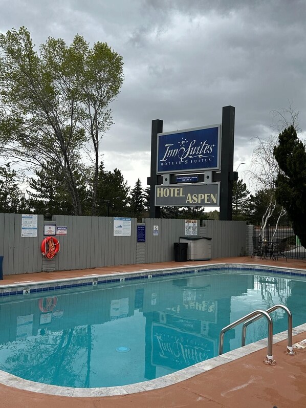 A swimming pool with a lifebuoy, a sign for Inn Suites Hotels & Suites, and a fence with various notices. - Hotel Aspen InnSuites Flagstaff/Grand Canyon (Flagstaff)