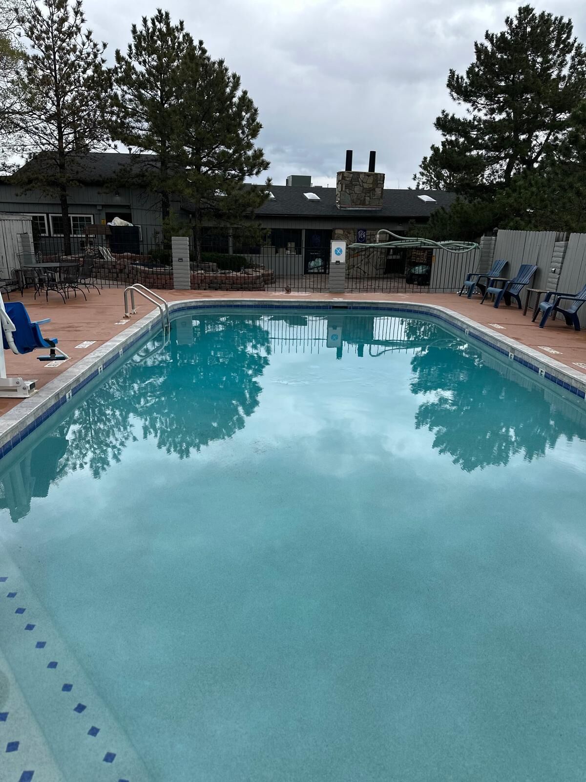 A rectangular swimming pool with clear blue water, surrounded by a tiled deck. There are lounge chairs and a covered seating area.