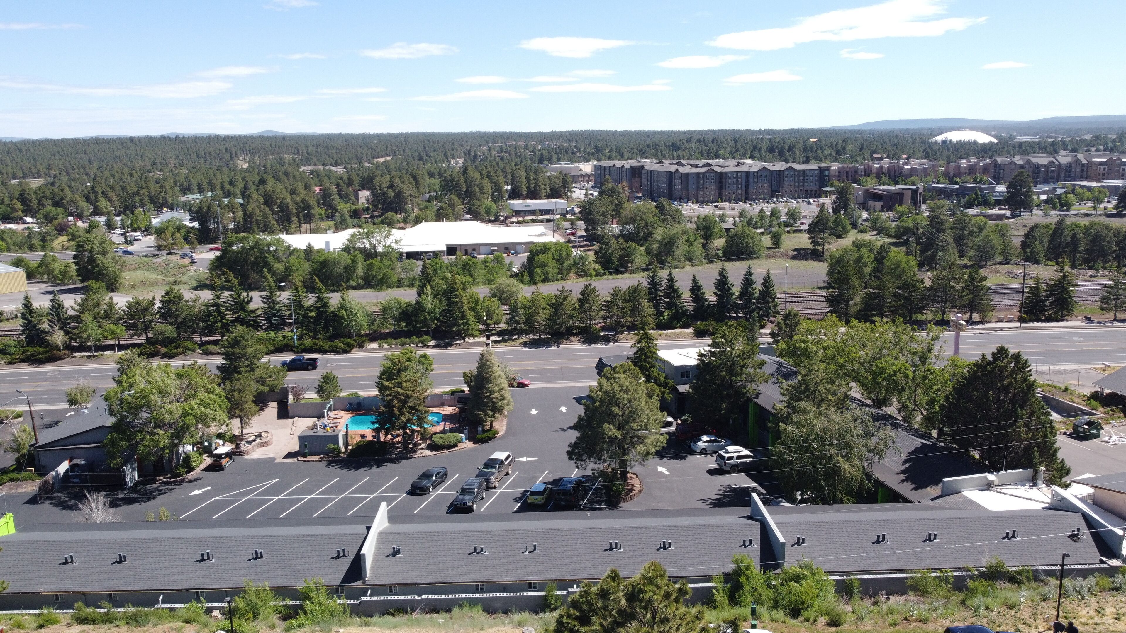 A parking lot with multiple rows of parking spaces, a swimming pool, and a building with a flat roof in the background.