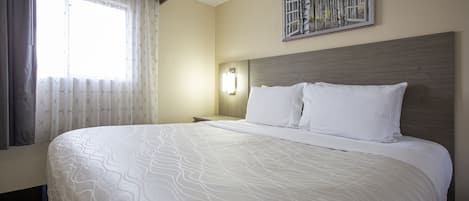 A hotel room with a large bed, a nightstand, a wall-mounted lamp, and a window with curtains.