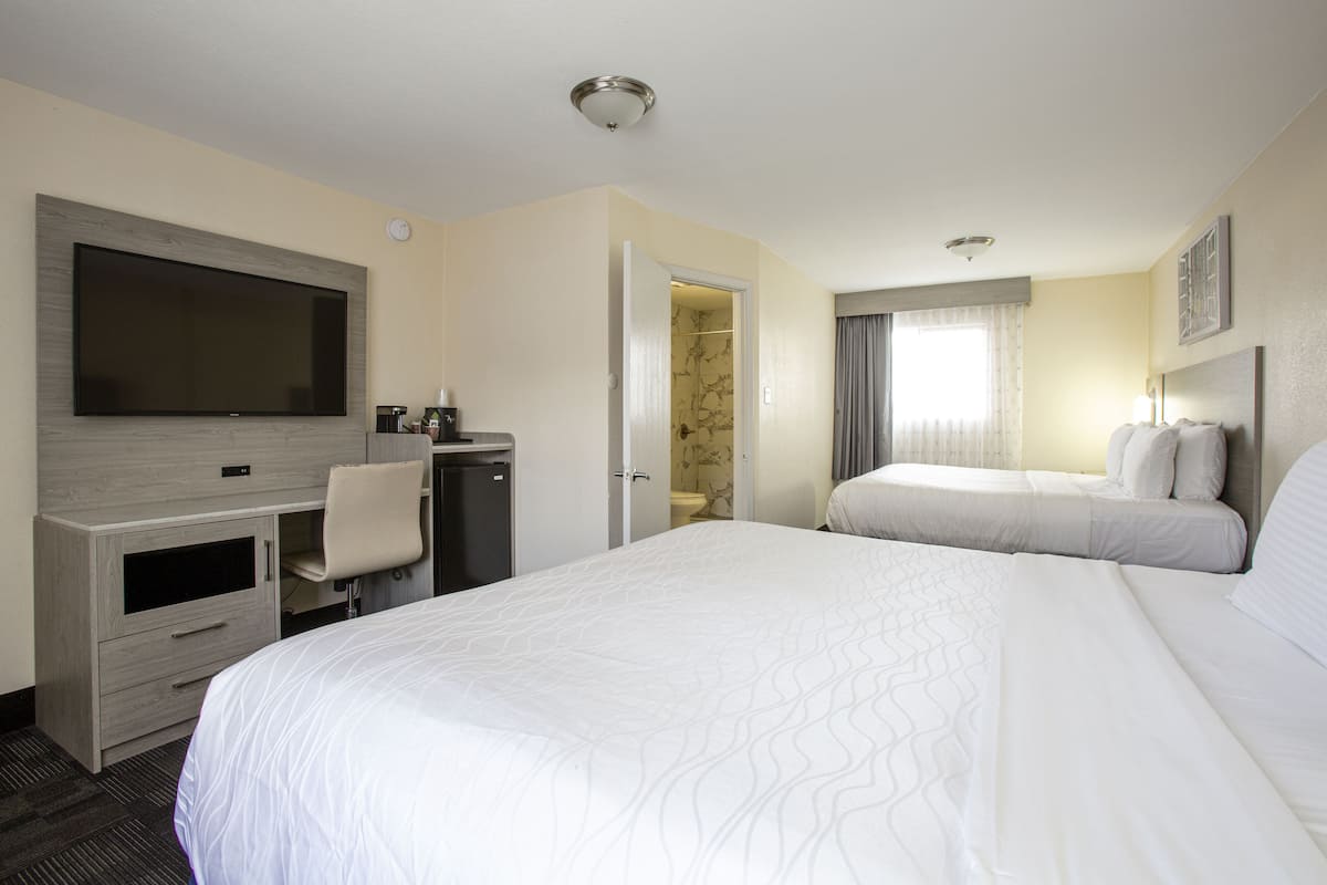 Habitación de hotel con una cama grande, un escritorio con televisor de pantalla plana, un armario y un baño visible a través de una puerta abierta.