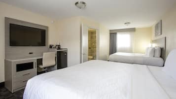 Habitación de hotel con una cama grande, un escritorio con televisor de pantalla plana, un armario y un baño visible a través de una puerta abierta.