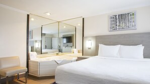 Una habitación de hotel moderna con una cama grande, una zona de estar, un baño con bañera y un espejo amplio.
