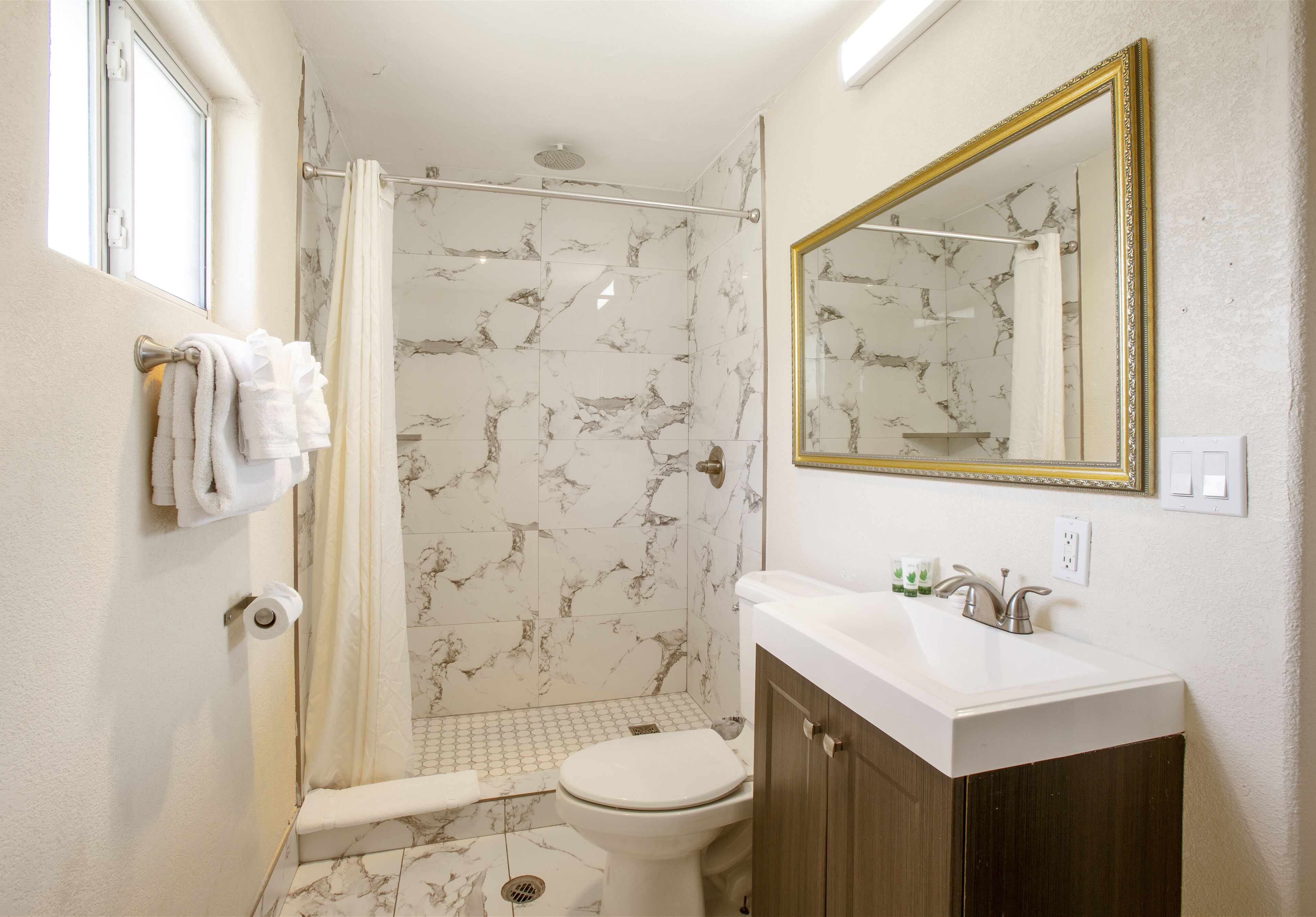 Une salle de bain équipée d’une douche, de toilettes, d’un lavabo et d’un miroir avec un cadre doré.