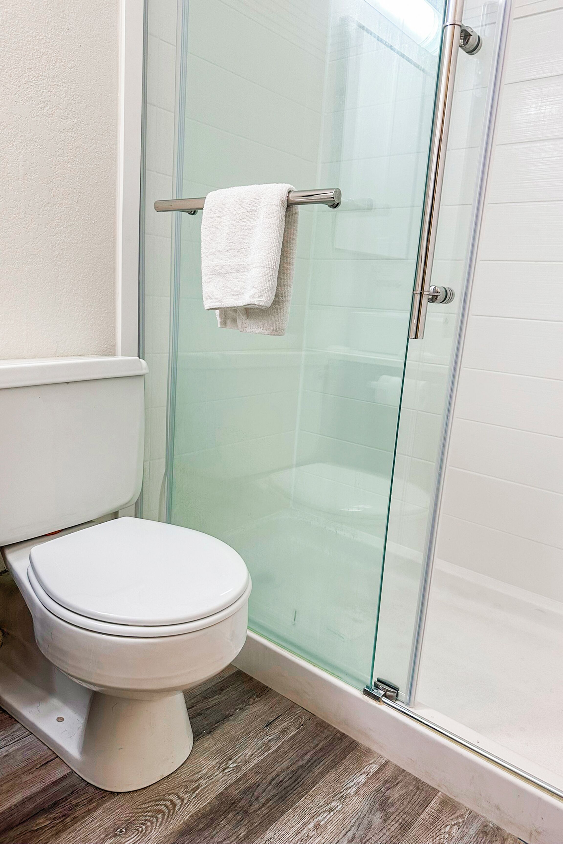 A bathroom with a glass shower enclosure, a white toilet, and a towel rack with a white towel.