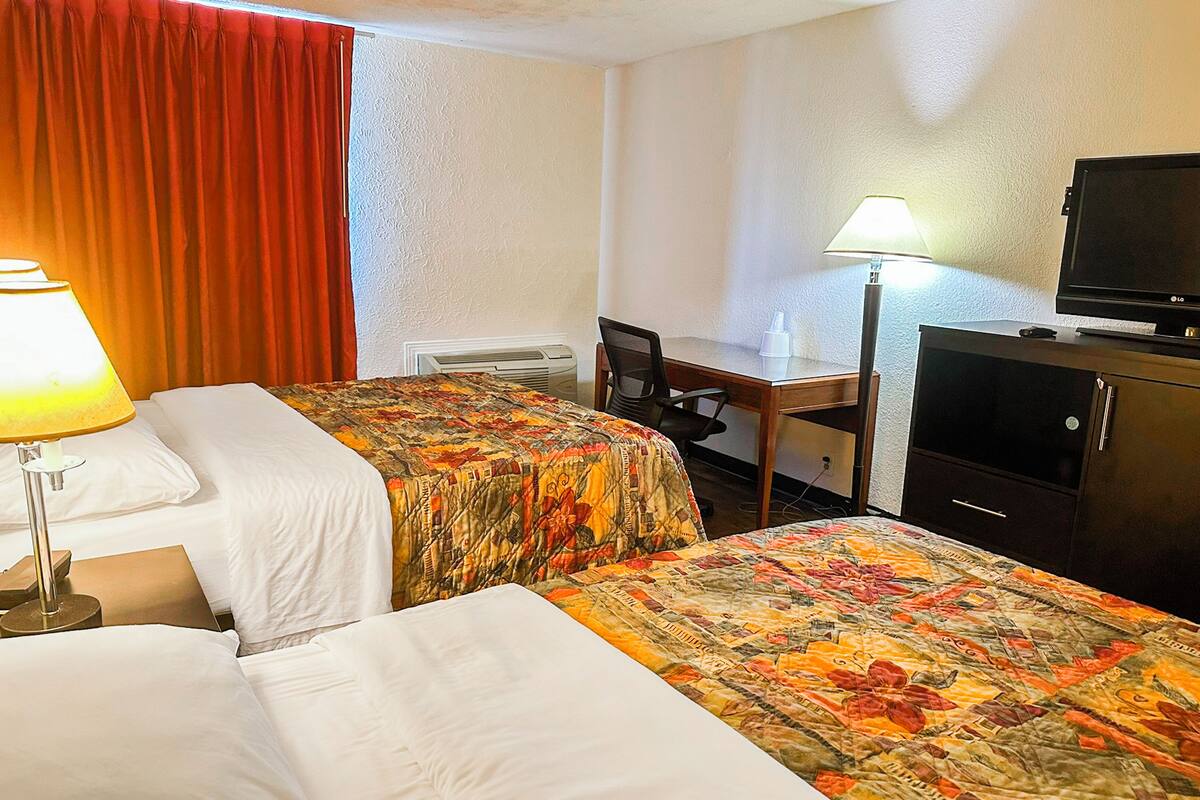 Ein Hotelzimmer mit zwei Betten, einem Schreibtisch, einem Fernseher und einer Lampe.