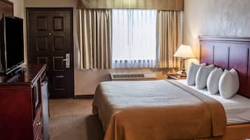 A hotel room with a bed, a television, a desk with a lamp, and a window with curtains.