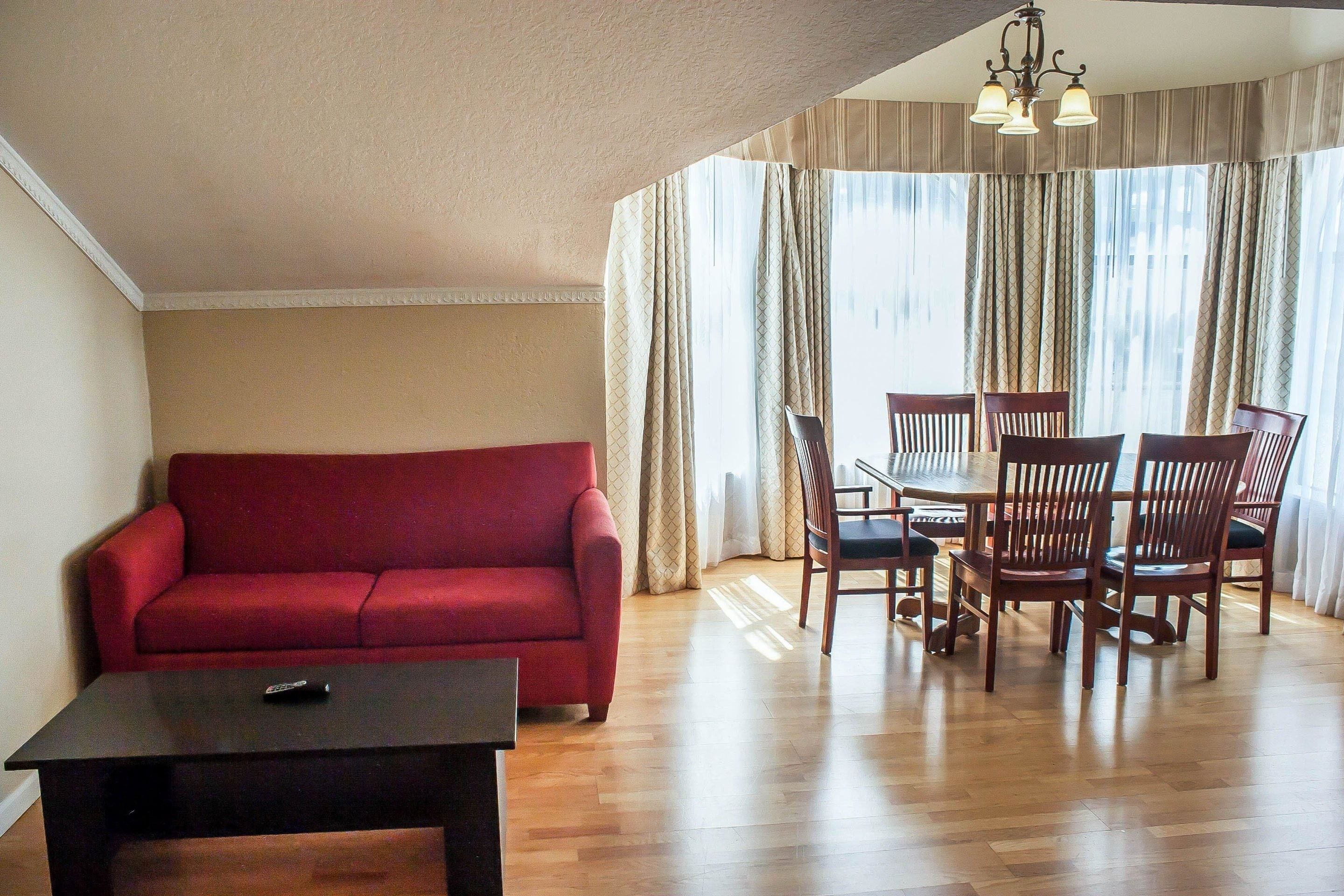 A living room with a red sofa, a dark coffee table, and a dining area with wooden chairs and a table.