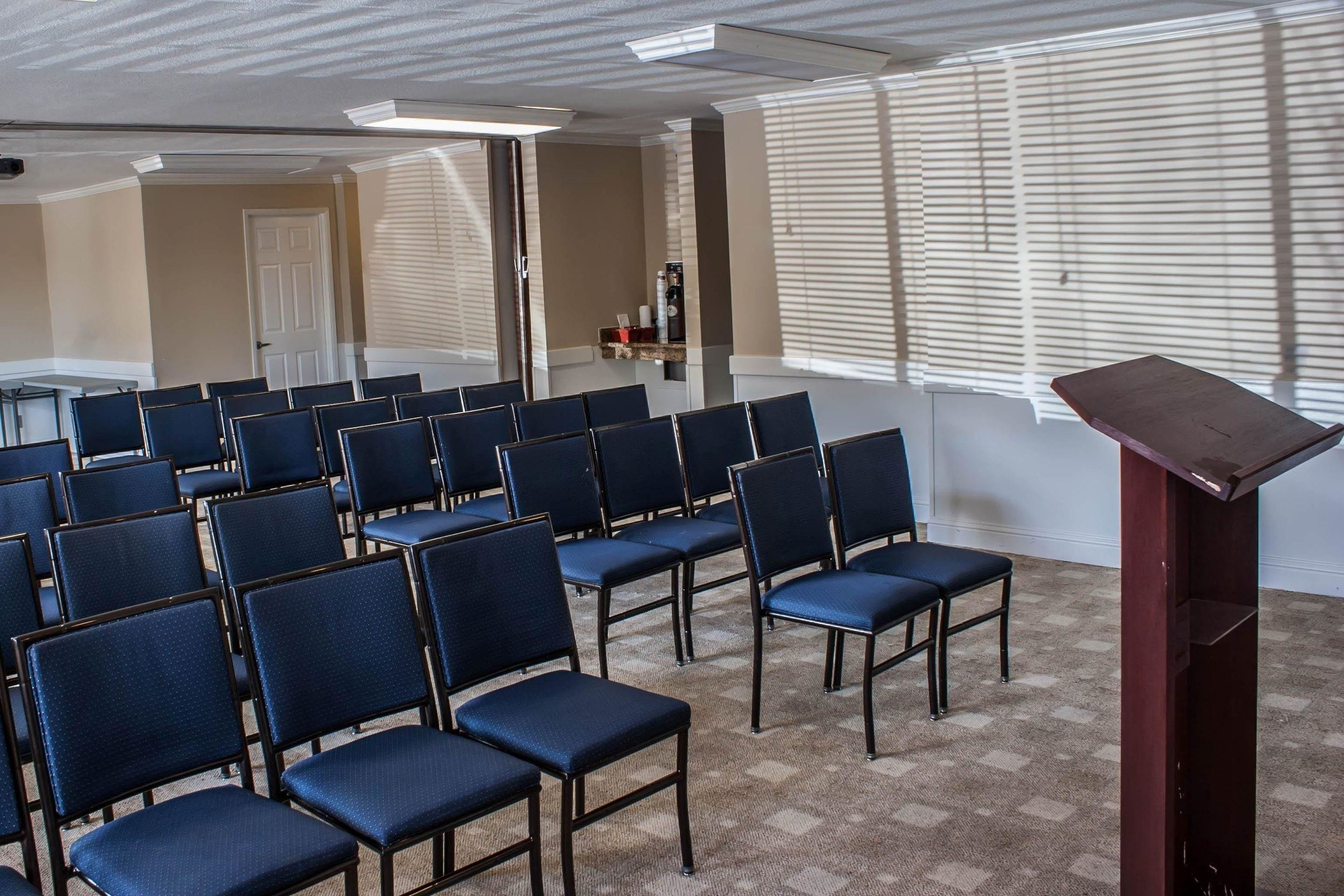 Un salón de conferencias con filas de sillas, un atril y una puerta al fondo.