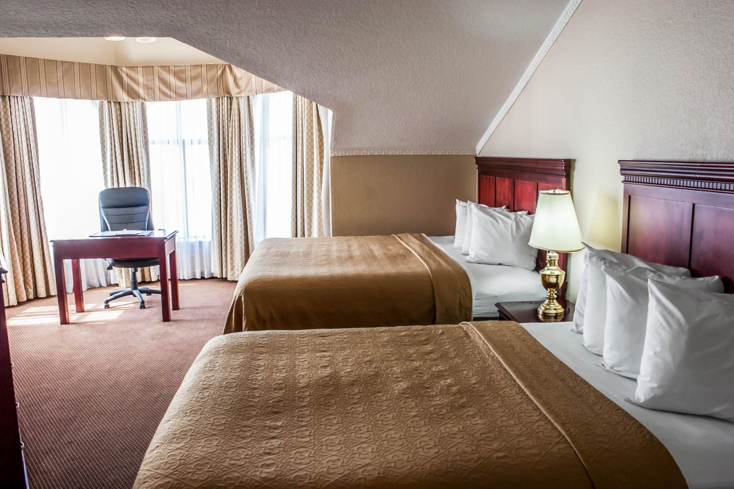A hotel room with two beds, a desk, and a chair.