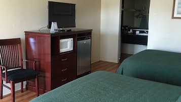 A hotel room with two beds, a desk with a television, a microwave, and a refrigerator.