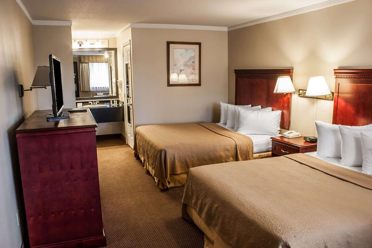 A hotel room with two beds, a desk with a television, a mirror, and a painting on the wall.