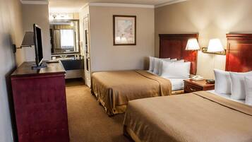 A hotel room with two beds, a desk with a TV, a mirror, and a painting on the wall.