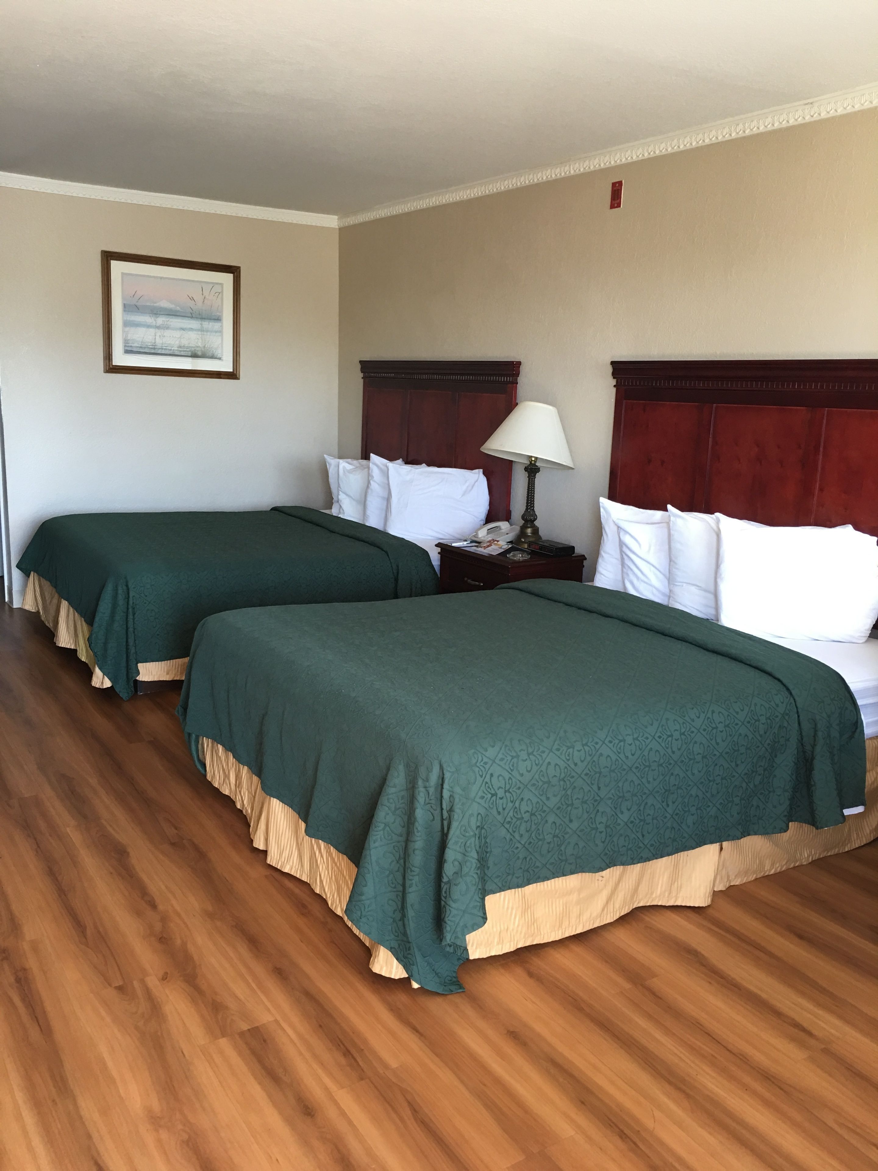 Une chambre d’hôtel avec deux lits, un plancher en bois, une table de chevet avec une lampe et un tableau encadré au mur.