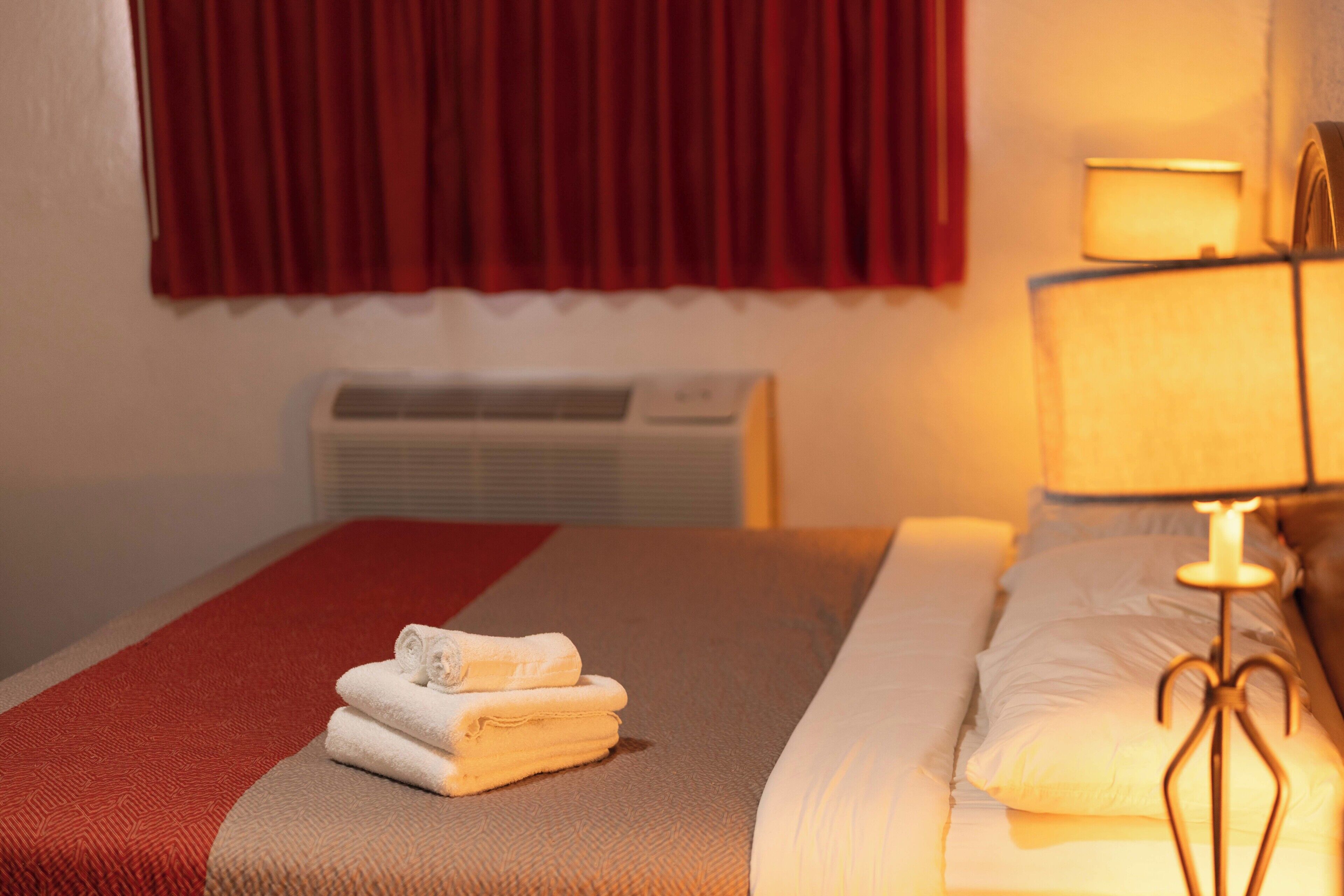 A hotel room with a bed, a red curtain, a wall-mounted air conditioner, and a bedside lamp.