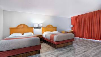 A hotel room with two beds, wooden headboards, bedside tables with lamps, and a red curtain.