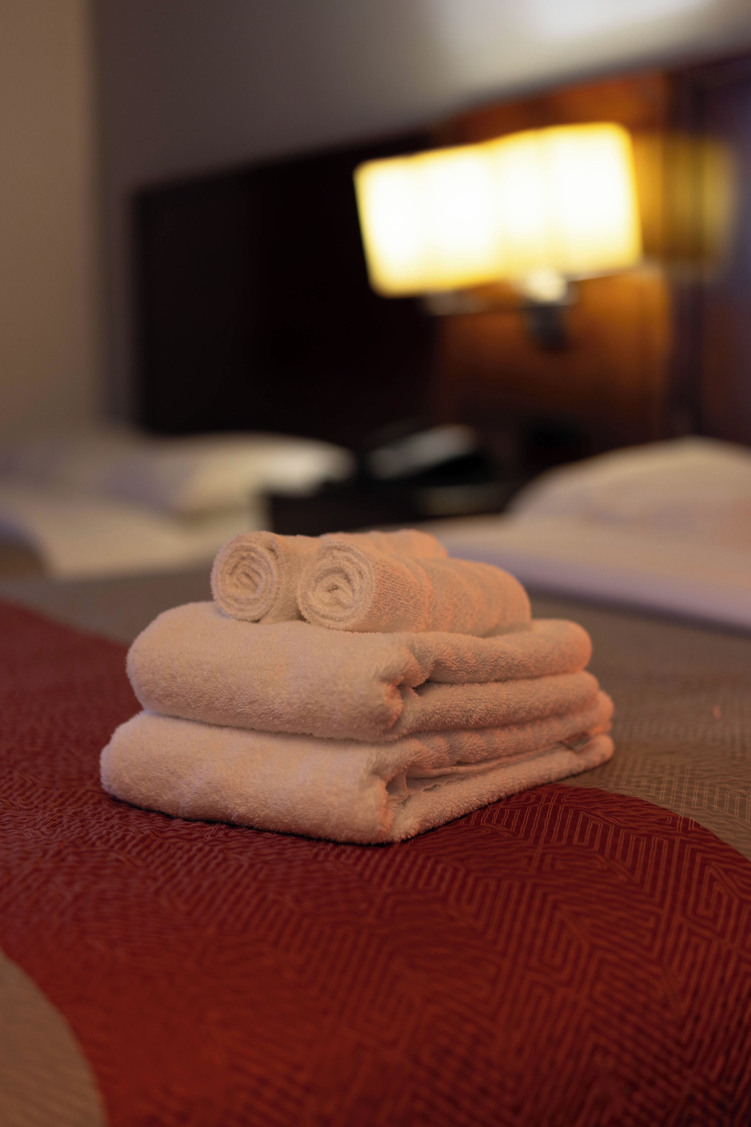 A stack of folded towels on a textured surface, with a blurred background featuring a lamp and a dark object.