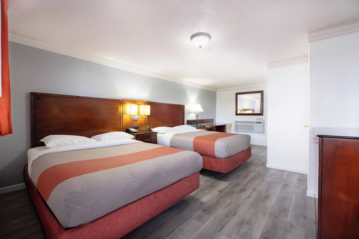 A hotel room with two beds, a wooden headboard, bedside lamps, a telephone, and a mirror on the wall.