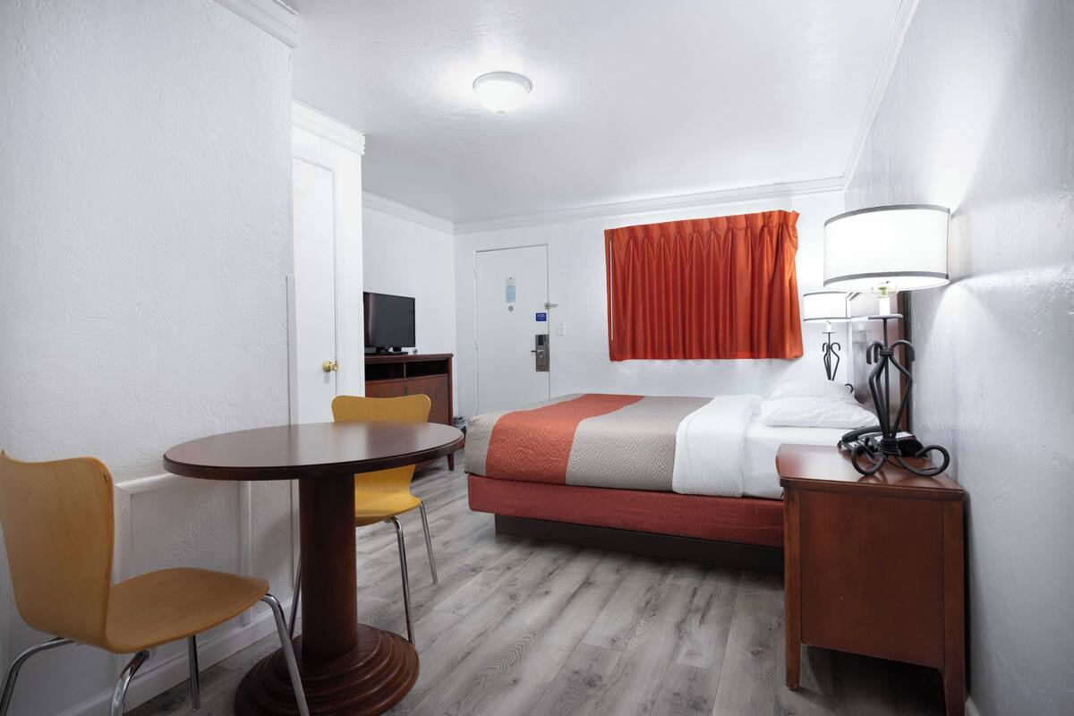 A hotel room with a bed, a desk, a chair, a lamp, and a television.
