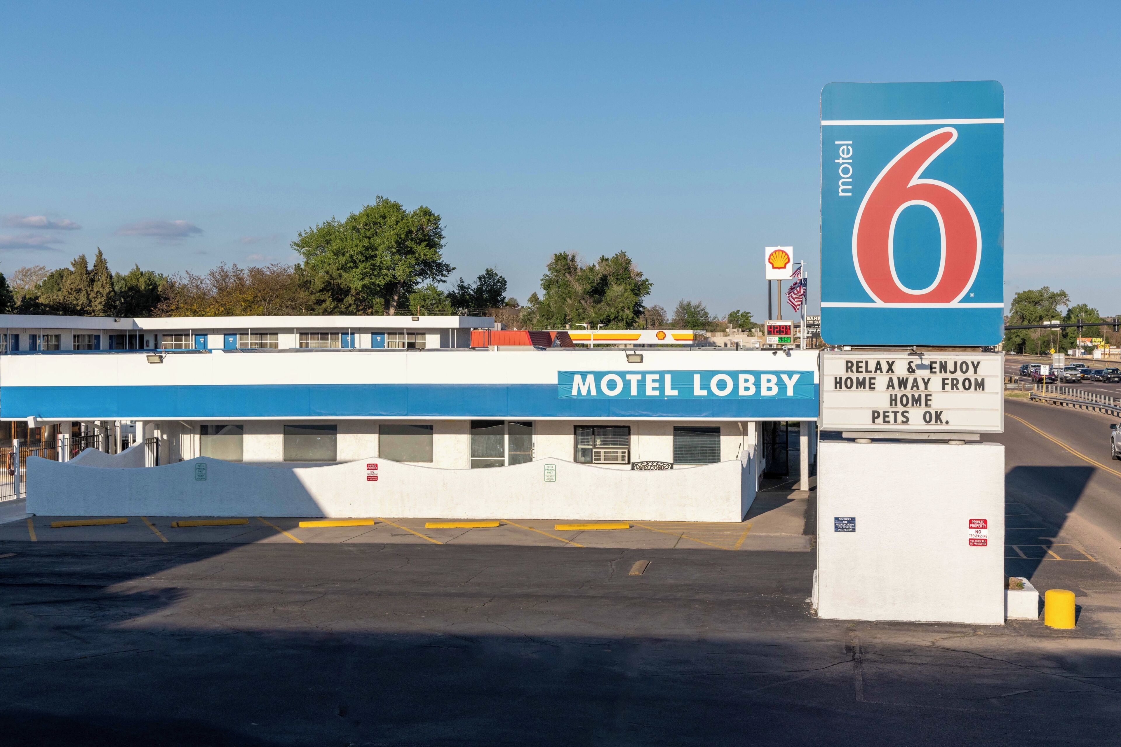 A motel with a blue and white exterior, a sign indicating it's number 6, and a slogan 'Relax & Enjoy Home Away from Home Pets OK.'