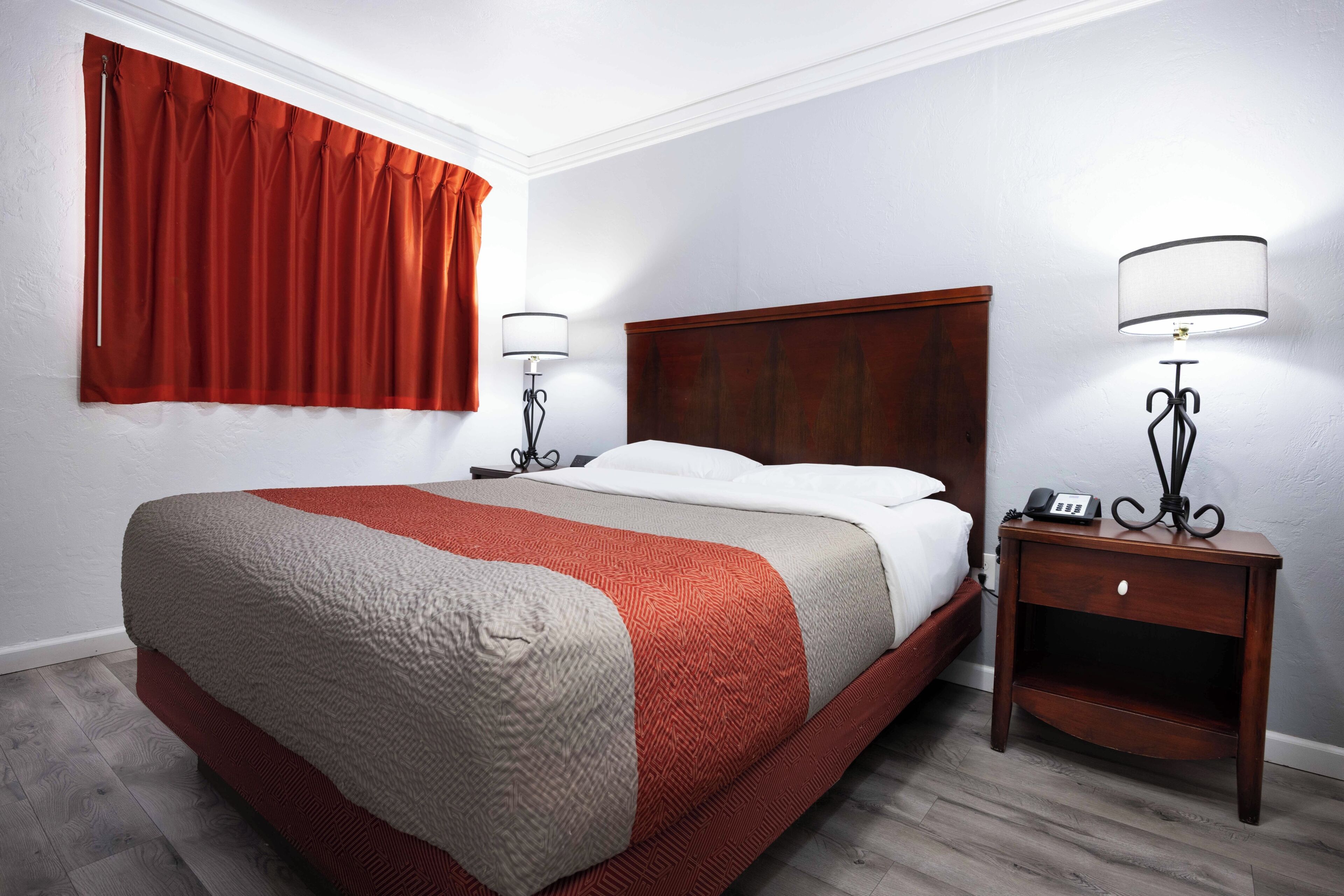 A hotel room with a bed, a nightstand with a lamp, and a window with curtains.