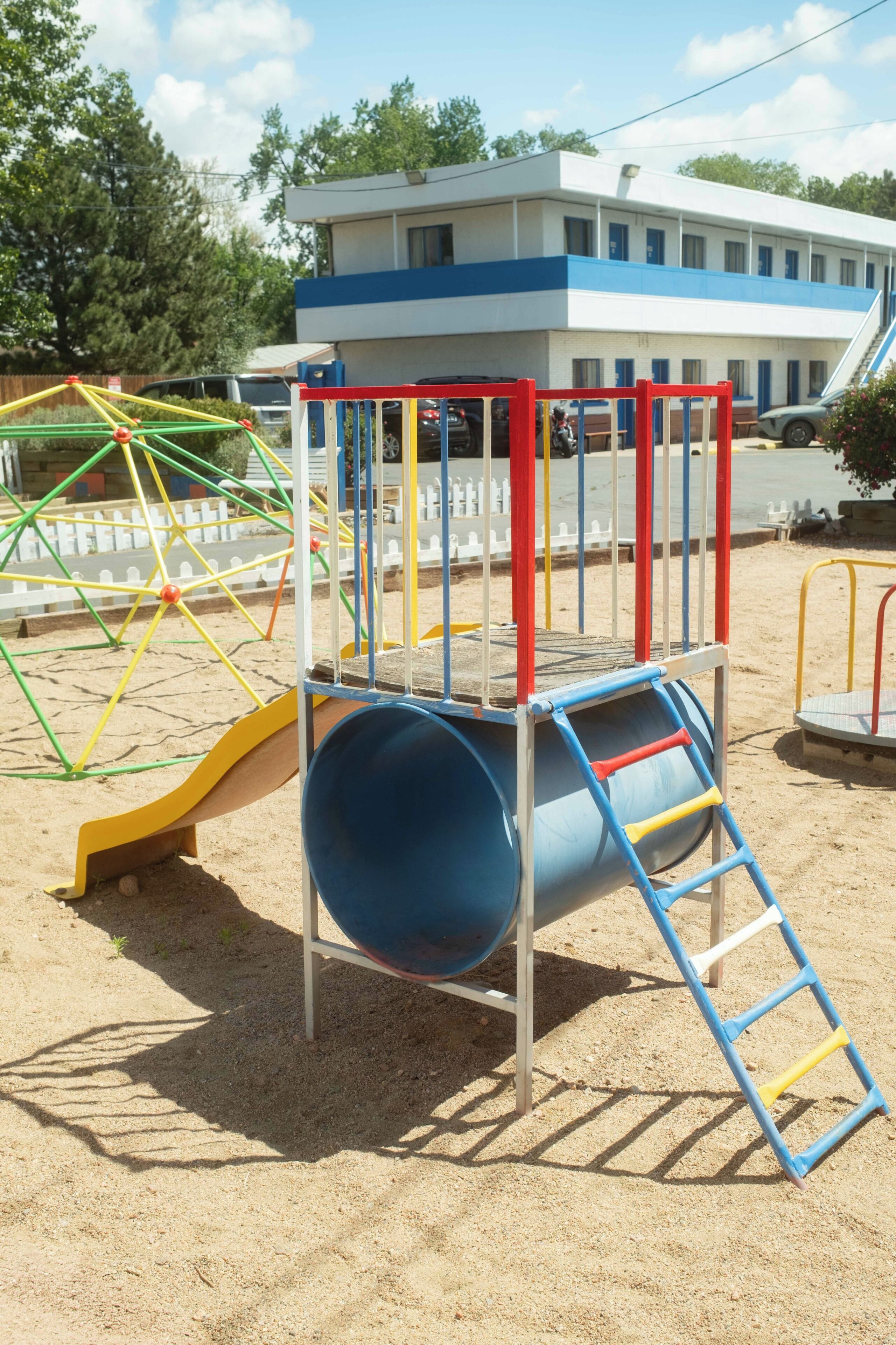 A playground with a slide, climbing structure, and a blue cylindrical play area.