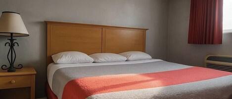 Un letto ben rifatto con poggiatesta in legno, un comodino con una lampada e una finestra con tende rosse.