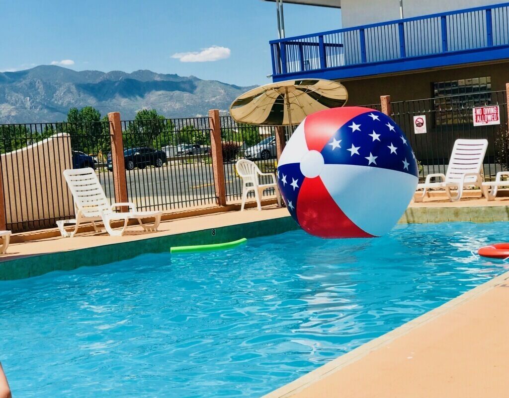 A pool with a beach ball, lounge chairs, and a view of mountains.